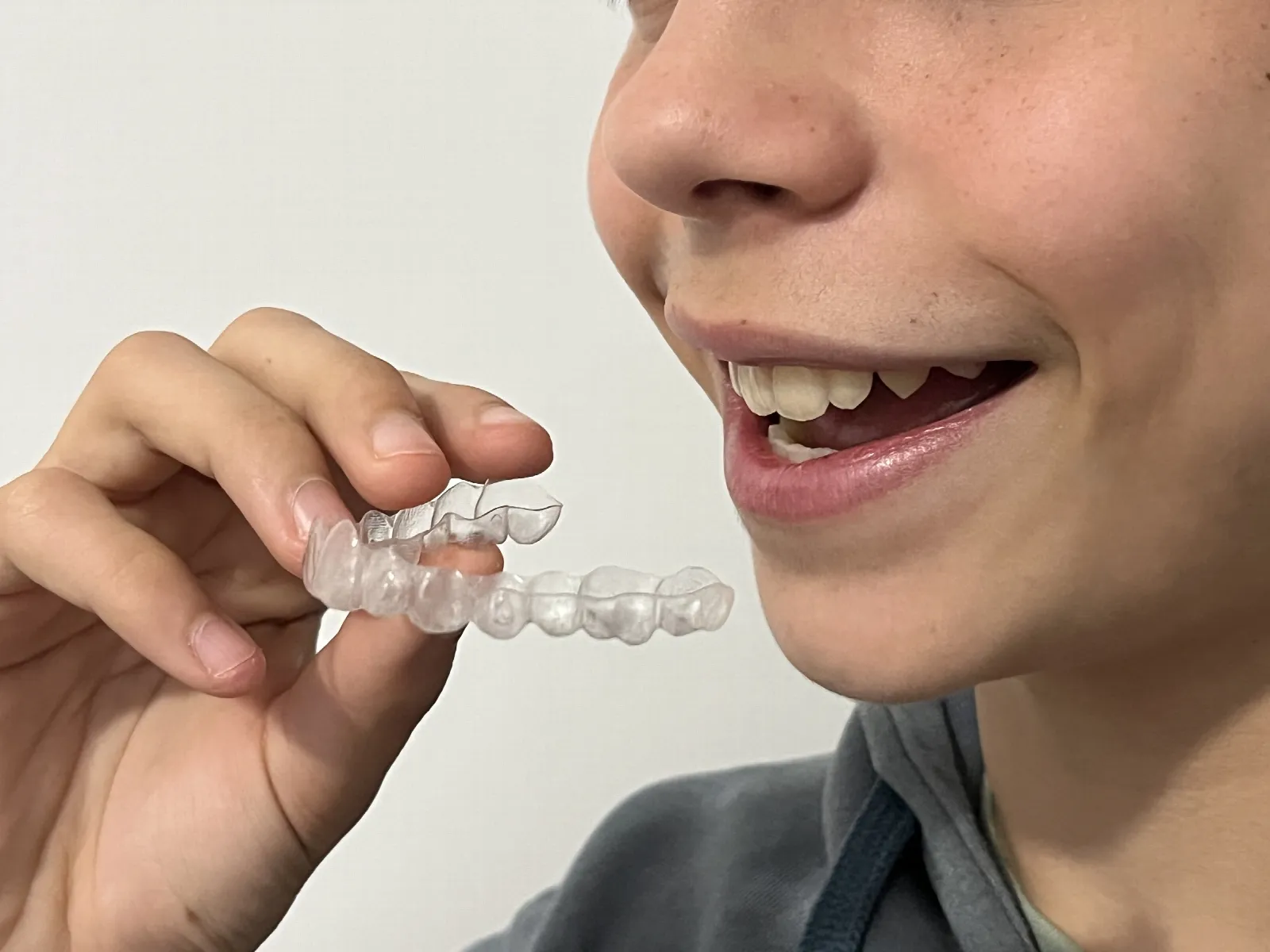 Una persona joven sonriendo mientras sostiene con los dedos un alineador transparente