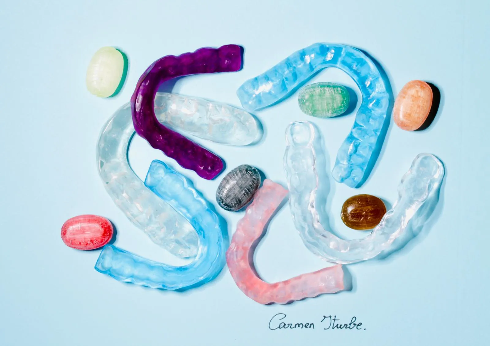 Varias férulas de descarga, transparentes y de colores (azul, morado, rosa), sobre un fondo azul claro y con caramelos de colores entre ellas; la foto lleva la firma de Carmen Iturbe